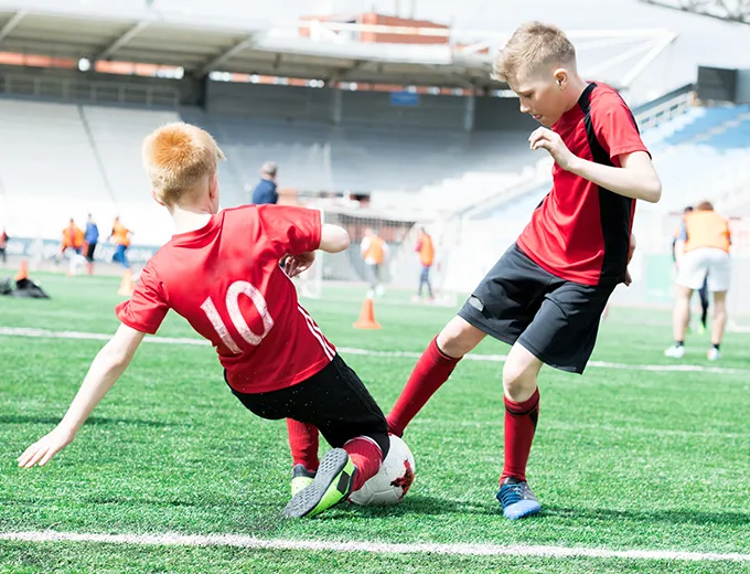 Two boys tackling each other with soccer ball between them